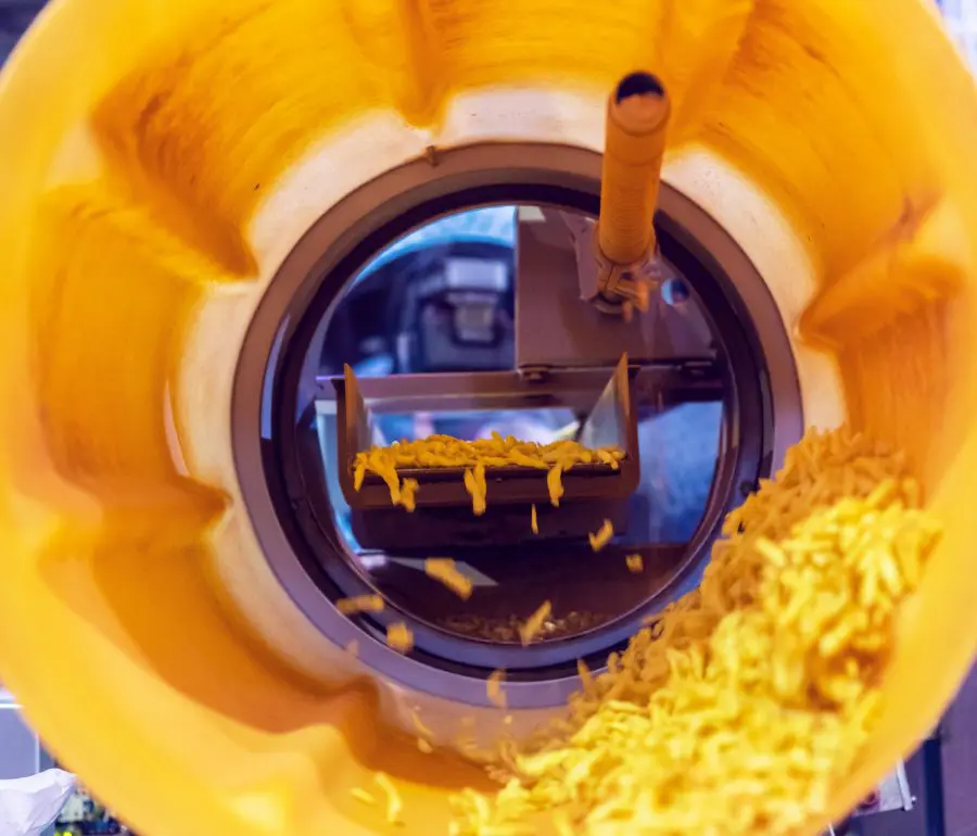 Corn snacks passing through a tumbling machine to support product uniformity.